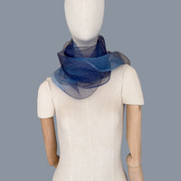 Mannequin wearing a colorful and lightweight silk scarf on a gray background. Silk scarf is in shades of gray, midnight blue and blue colors. It is hand-painted scarf in measures 50 x 200 cm by otta-italy scarves brand.
