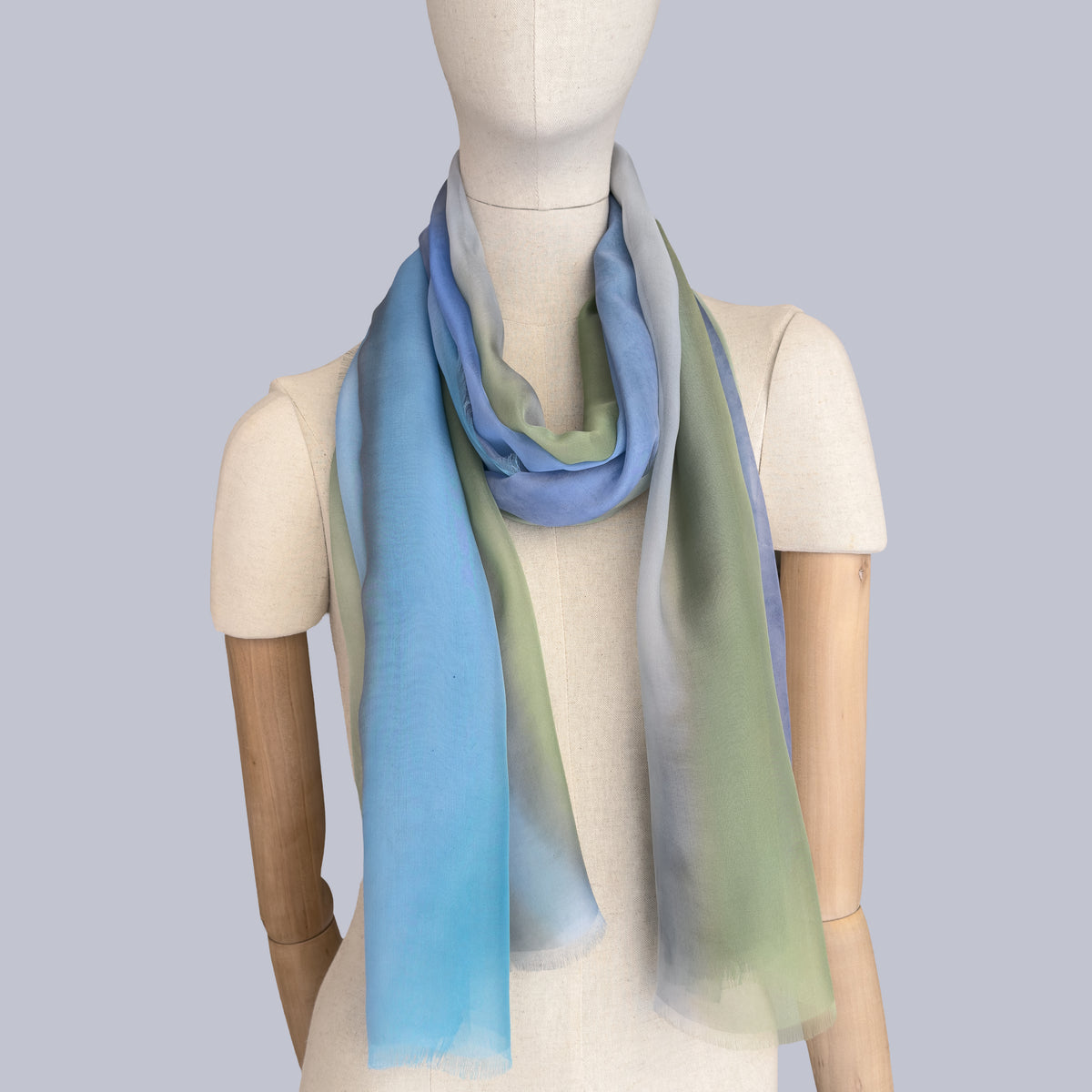 Mannequin wearing scarf on a gray background. Hand-painted silk scarf by Otta-Italy, 65 x 175 cm, featuring 
blue, green and gray. Luxury Italian pure silk accessory, soft, fresh and lightweight scarf for women and men.
