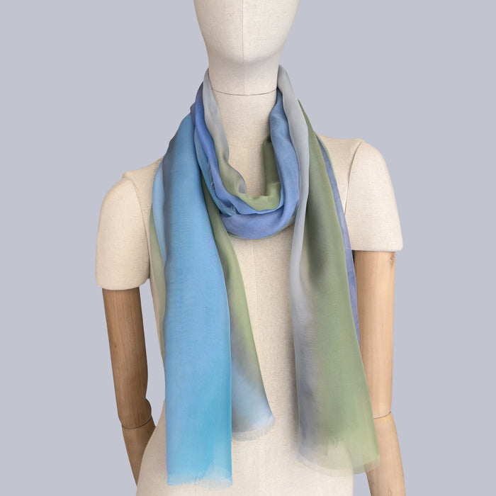 Mannequin wearing scarf on a gray background. Hand-painted silk scarf by Otta-Italy, 65 x 175 cm, featuring 
blue, green and gray. Luxury Italian pure silk accessory, soft, fresh and lightweight scarf for women and men.
