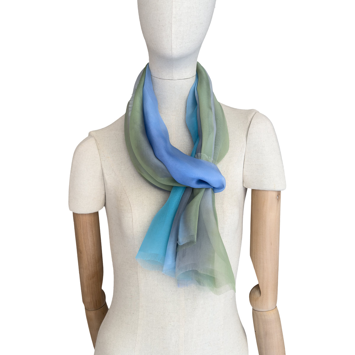 Mannequin wearing a hand-painted Otta pure silk scarf on a white background in 
blue, green and gray tones. soft, fresh and lightweight, and elegant accessory measuring 65 x 175 cm. Unique artisan scarf with hand-fringed edges, perfect for women and men.
