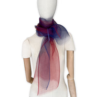 Mannequin wearing a colorful and lightweight silk scarf on a white background. Silk scarf is in shades of red and blue colors. It is hand-painted scarf in measures 48 x 194 cm by otta-italy scarves brand.