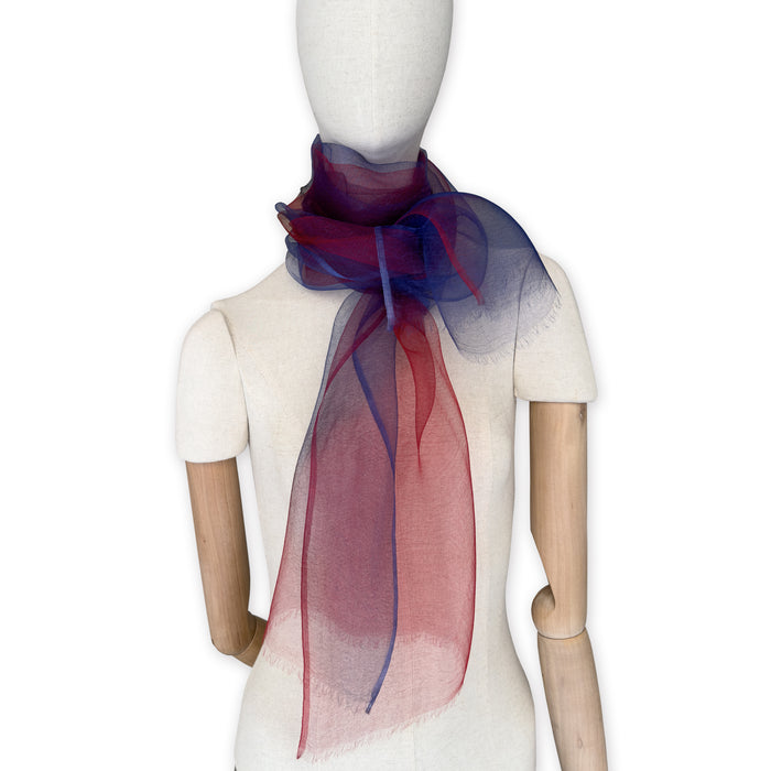 Mannequin wearing a colorful and lightweight silk scarf on a white background. Silk scarf is in shades of red and blue colors. It is hand-painted scarf in measures 48 x 194 cm by otta-italy scarves brand.