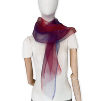 Mannequin wearing a colorful and lightweight silk scarf on a white background. Silk scarf is in shades of red and blue colors. It is hand-painted scarf in measures 48 x 194 cm by otta-italy scarves brand.