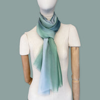 Mannequin wearing scarf on a gray background. Hand-painted silk scarf by Otta-Italy, 65 x 175 cm, featuring 
green and blue. Luxury Italian pure silk accessory, soft, fresh and lightweight scarf for women and men.
