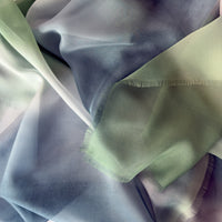 Close-up of a hand-painted Otta pure silk scarf draped softly, showcasing gentle shades of 
green and blue. Lightweight artisan accessory with delicate hand-fringed edges, measuring 65 x 175 cm.
