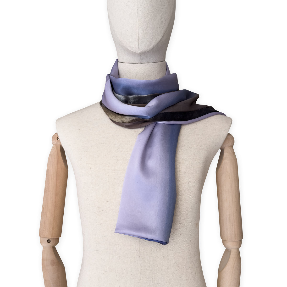 Mannequin wearing a colorful and lightweight silk scarf on a white background. Silk scarf is in shades of blue, lilac and brown colors. It is hand-painted scarf in measures 171 x 24 cm by otta-italy scarves brand.
