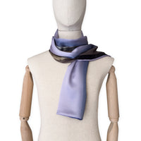 Mannequin wearing a colorful and lightweight silk scarf on a white background. Silk scarf is in shades of blue, lilac and brown colors. It is hand-painted scarf in measures 171 x 24 cm by otta-italy scarves brand.
