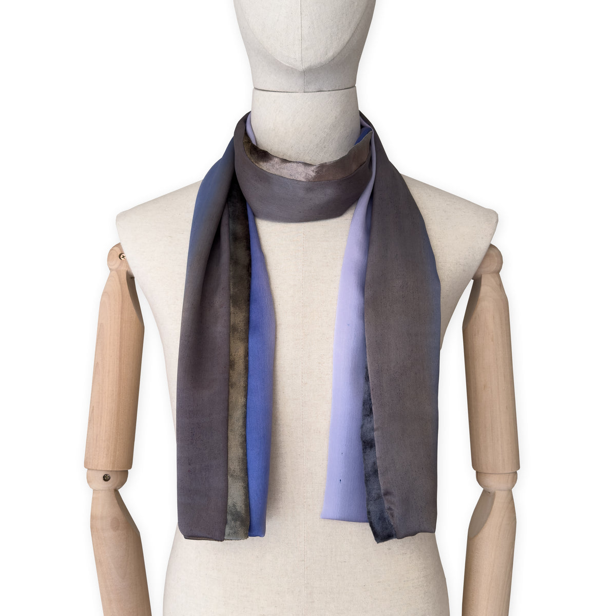 Mannequin wearing a colorful and lightweight silk scarf on a white background. Silk scarf is in shades of blue, lilac and brown colors. It is hand-painted scarf in measures 171 x 24 cm by otta-italy scarves brand.
