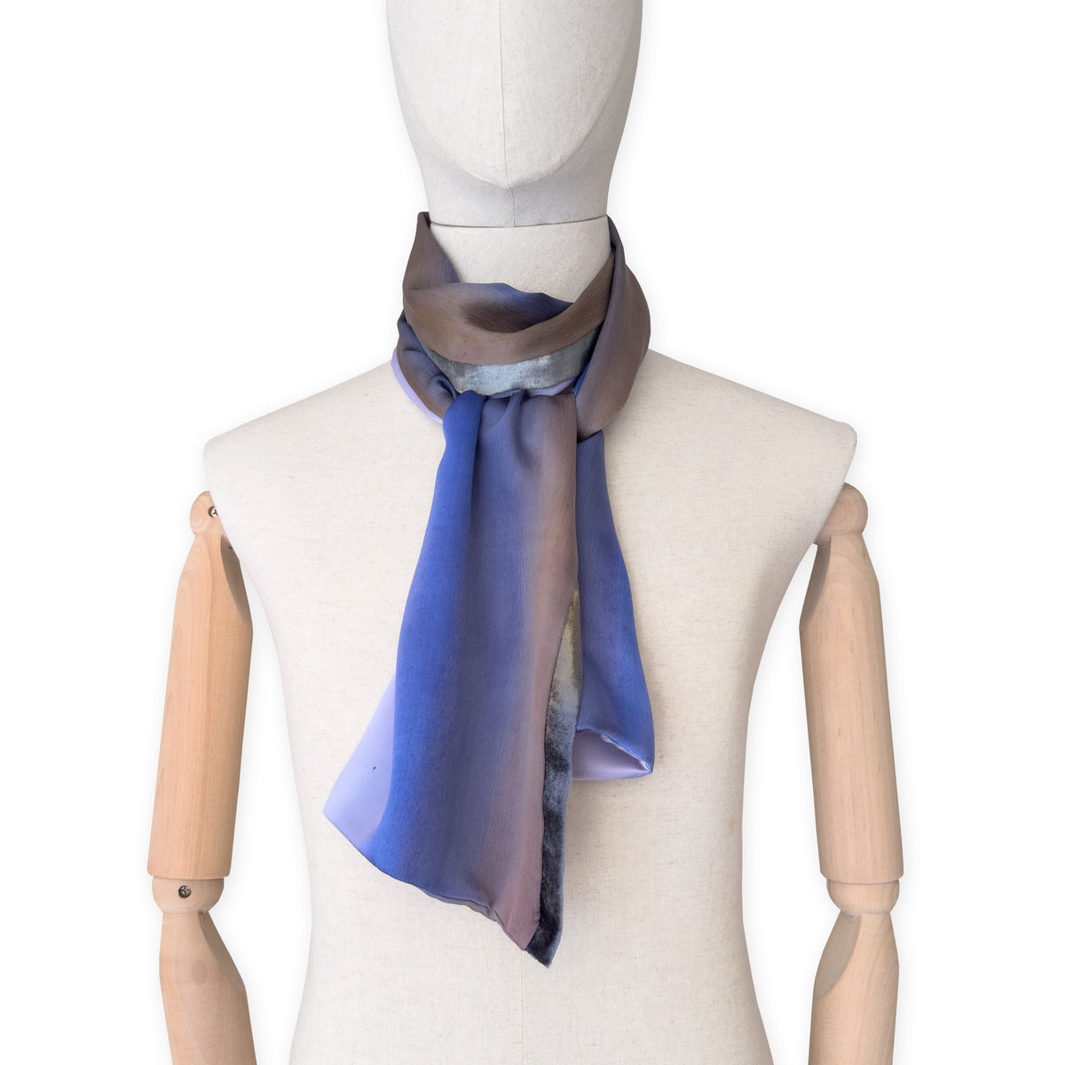 Mannequin wearing a colorful and lightweight silk scarf on a white background. Silk scarf is in shades of blue, lilac and brown colors. It is hand-painted scarf in measures 171 x 24 cm by otta-italy scarves brand.
