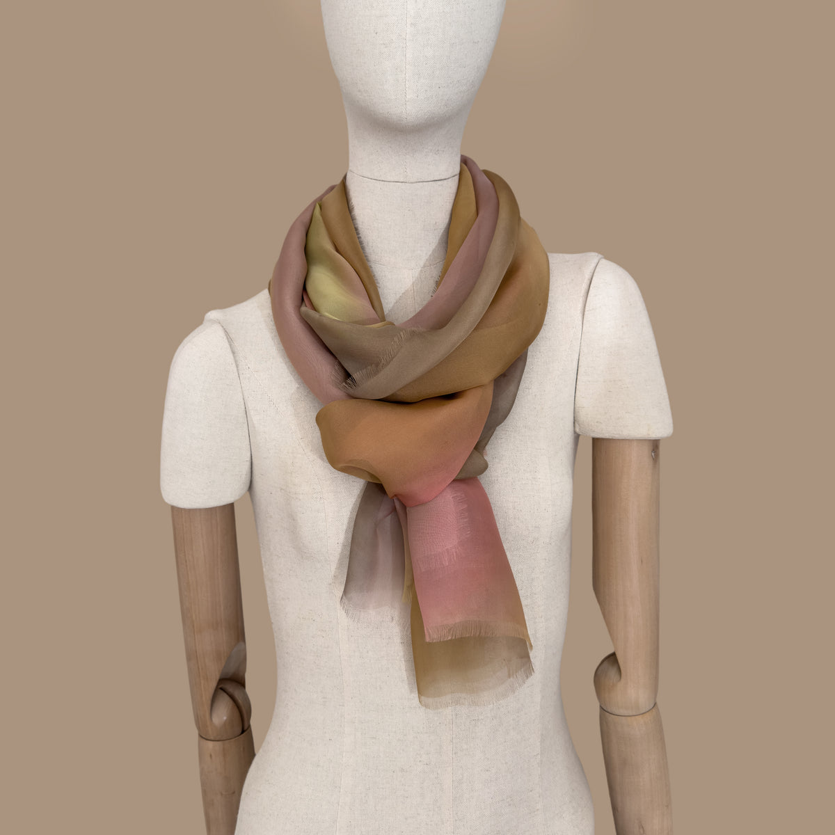 Mannequin wearing scarf on a beige background. Hand-painted silk scarf by Otta-Italy, 65 x 175 cm, featuring 
pink, yellow and brown. Luxury Italian pure silk accessory, soft, fresh and lightweight scarf for women and men.
