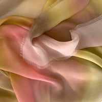 Close-up of a hand-painted Otta pure silk scarf draped softly, showcasing gentle shades of 
pink, yellow and brown. Lightweight artisan accessory with delicate hand-fringed edges, measuring 65 x 175 cm.
