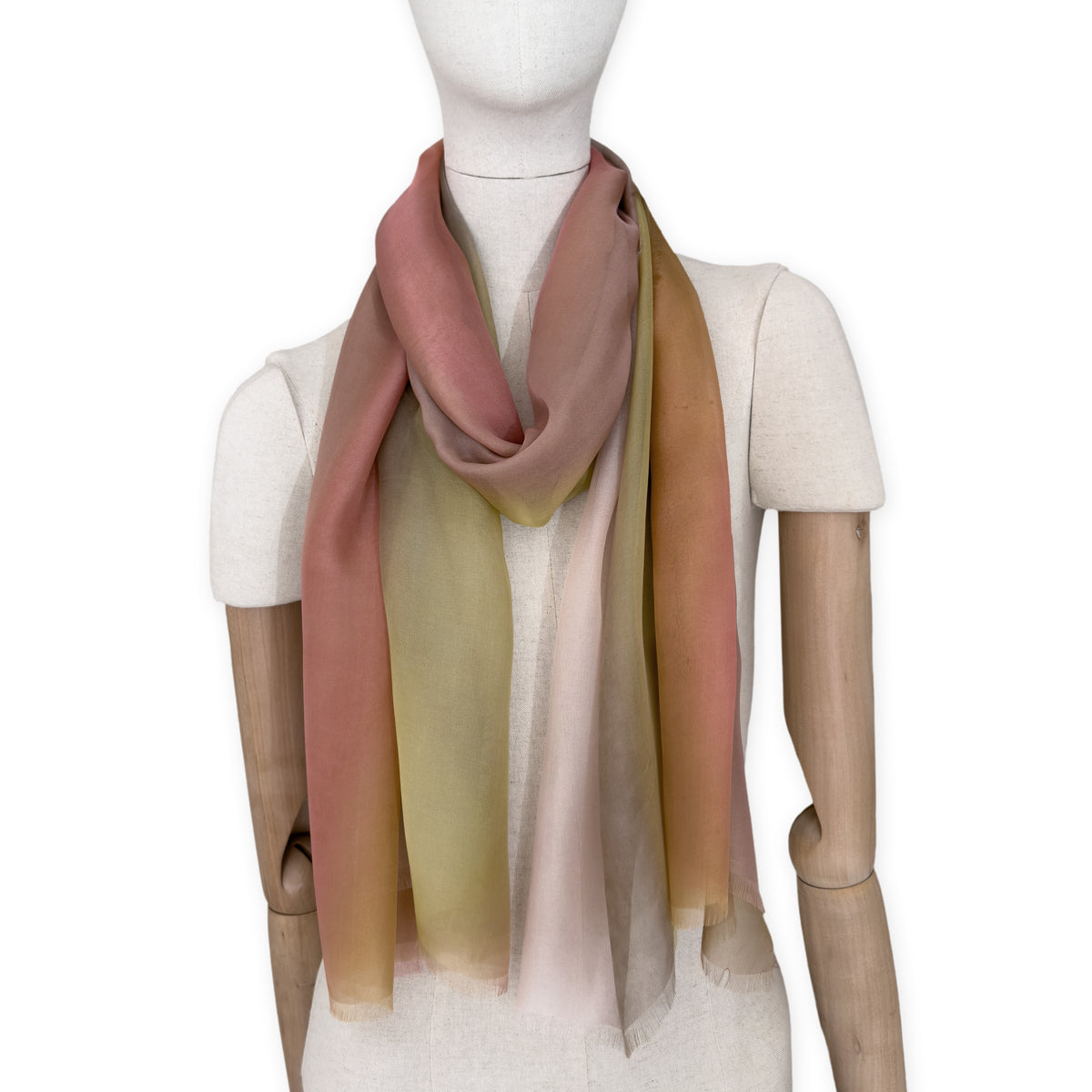 Mannequin wearing a hand-painted Otta pure silk scarf on a white background in 
pink, yellow and brown tones. soft, fresh and lightweight, and elegant accessory measuring 65 x 175 cm. Unique artisan scarf with hand-fringed edges, perfect for women and men.
