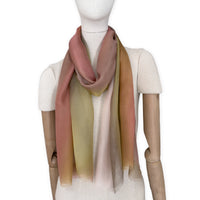 Mannequin wearing a hand-painted Otta pure silk scarf on a white background in 
pink, yellow and brown tones. soft, fresh and lightweight, and elegant accessory measuring 65 x 175 cm. Unique artisan scarf with hand-fringed edges, perfect for women and men.

