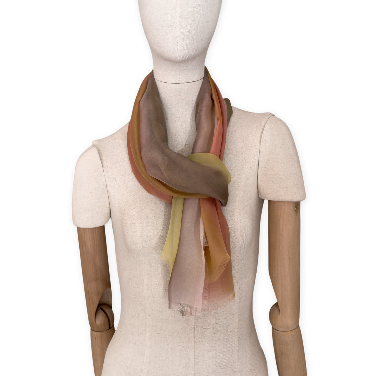 Mannequin wearing a hand-painted Otta pure silk scarf on a white background in 
pink, yellow and brown tones. soft, fresh and lightweight, and elegant accessory measuring 65 x 175 cm. Unique artisan scarf with hand-fringed edges, perfect for women and men.
