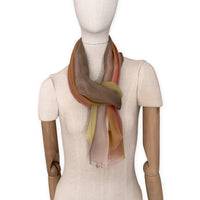 Mannequin wearing a hand-painted Otta pure silk scarf on a white background in 
pink, yellow and brown tones. soft, fresh and lightweight, and elegant accessory measuring 65 x 175 cm. Unique artisan scarf with hand-fringed edges, perfect for women and men.
