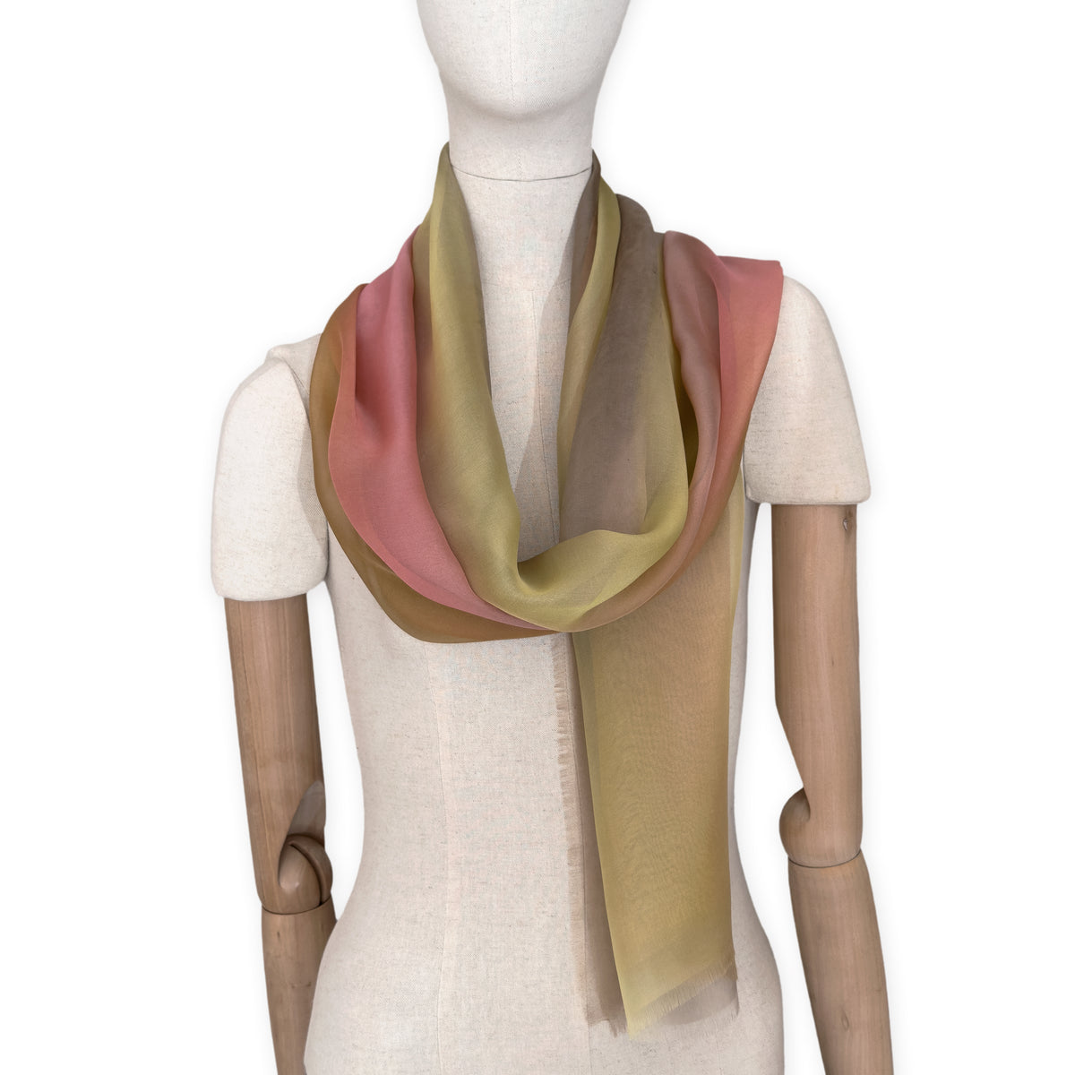Mannequin wearing a hand-painted Otta pure silk scarf on a white background in 
pink, yellow and brown tones. soft, fresh and lightweight, and elegant accessory measuring 65 x 175 cm. Unique artisan scarf with hand-fringed edges, perfect for women and men.

