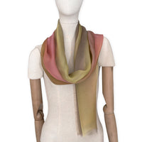 Mannequin wearing a hand-painted Otta pure silk scarf on a white background in 
pink, yellow and brown tones. soft, fresh and lightweight, and elegant accessory measuring 65 x 175 cm. Unique artisan scarf with hand-fringed edges, perfect for women and men.
