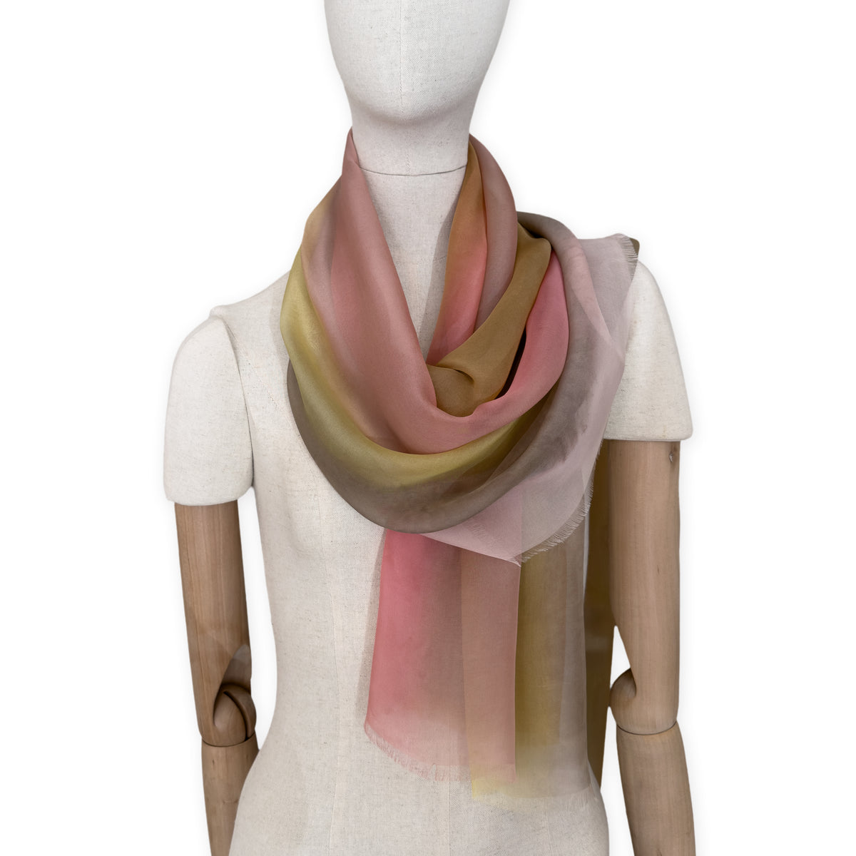 Mannequin wearing a hand-painted Otta pure silk scarf on a white background in 
pink, yellow and brown tones. soft, fresh and lightweight, and elegant accessory measuring 65 x 175 cm. Unique artisan scarf with hand-fringed edges, perfect for women and men.
