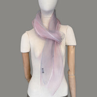 Mannequin wearing a hand-painted Otta silk scarf on a gray background in 
pink and light gray tones. Lightweight, soft, and elegant accessory measuring 50 x 200 cm. Unique artisan scarf with hand-fringed edges, perfect for women and men.
