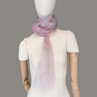 Mannequin wearing a hand-painted Otta silk scarf on a gray background in 
pink and light gray tones. Lightweight, soft, and elegant accessory measuring 50 x 200 cm. Unique artisan scarf with hand-fringed edges, perfect for women and men.
