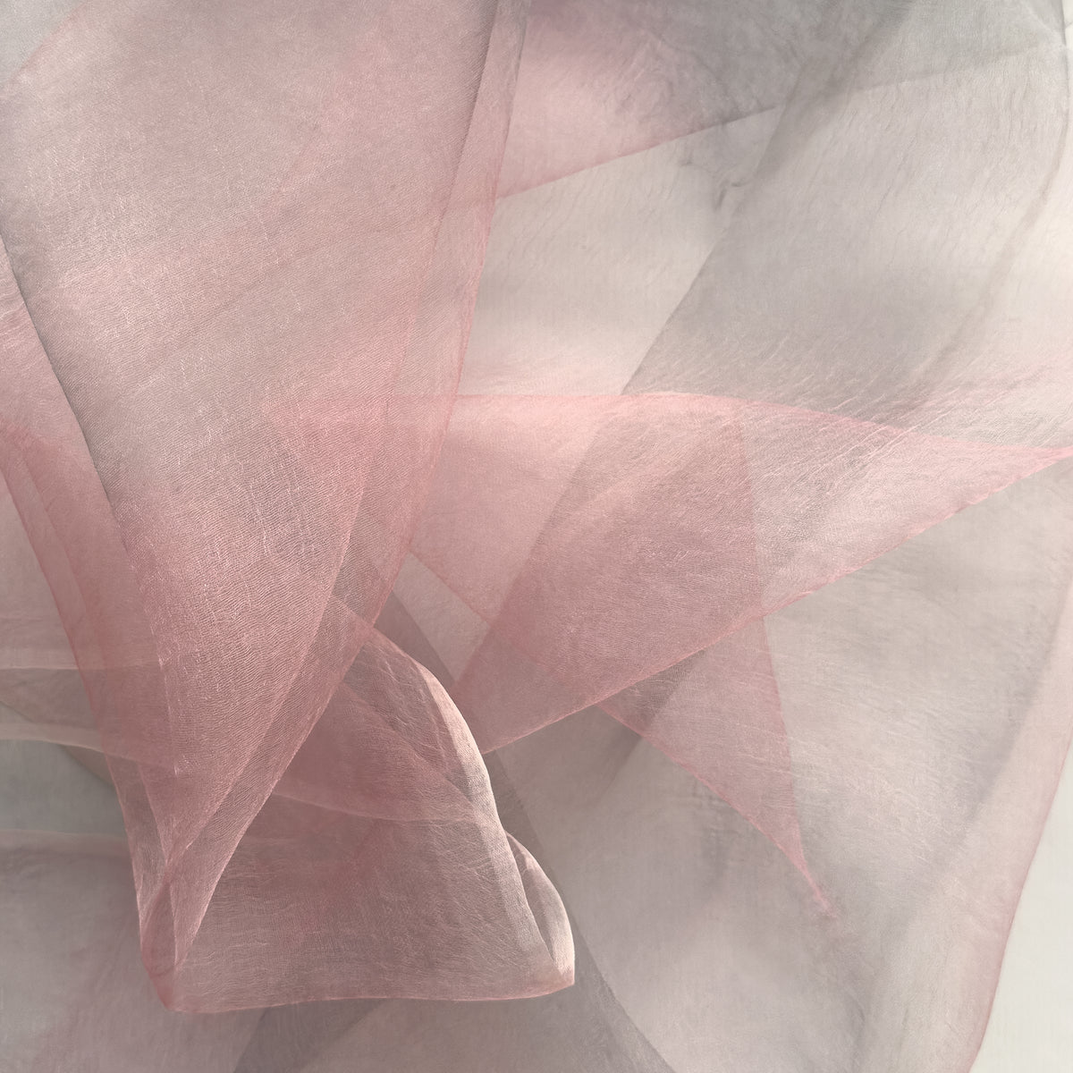 Close-up of a hand-painted Otta silk scarf draped softly, showcasing gentle shades of 
pink and light gray. Lightweight artisan accessory with delicate hand-fringed edges, measuring 50 x 200 cm.


