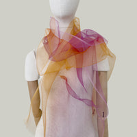 Mannequin wearing a hand-painted pure silk organza scarf by Otta-Italy, gray background. Orange, red and pink. 48x185 cm.

