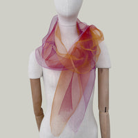 Mannequin wearing an elegant hand-painted Otta pure silk organza scarf on a gray background. Orange, red and pink tones.
