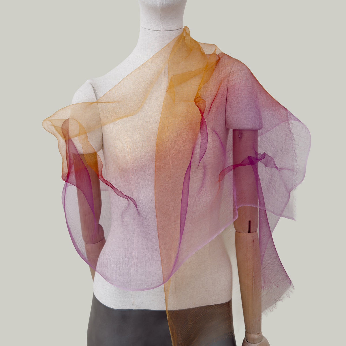 Mannequin wearing an elegant hand-painted Otta pure silk organza scarf on a gray background. Orange, red and pink tones.
