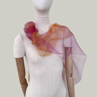 Mannequin wearing an elegant hand-painted Otta pure silk organza scarf on a gray background. Orange, red and pink tones.
