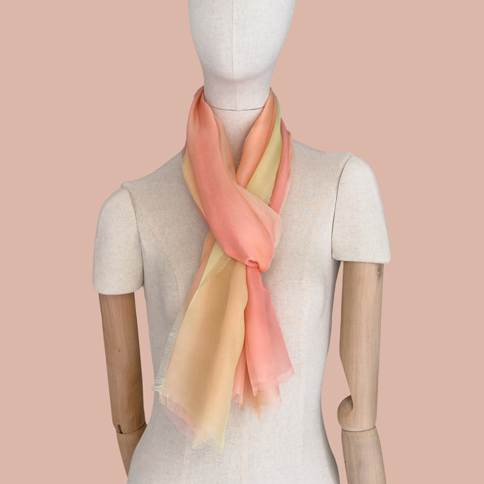 Mannequin wearing scarf on a beige background. Hand-painted silk scarf by Otta-Italy, 65 x 175 cm, featuring 
coral, peach, yellow and light green. Luxury Italian pure silk accessory, soft, fresh and lightweight scarf for women and men.
