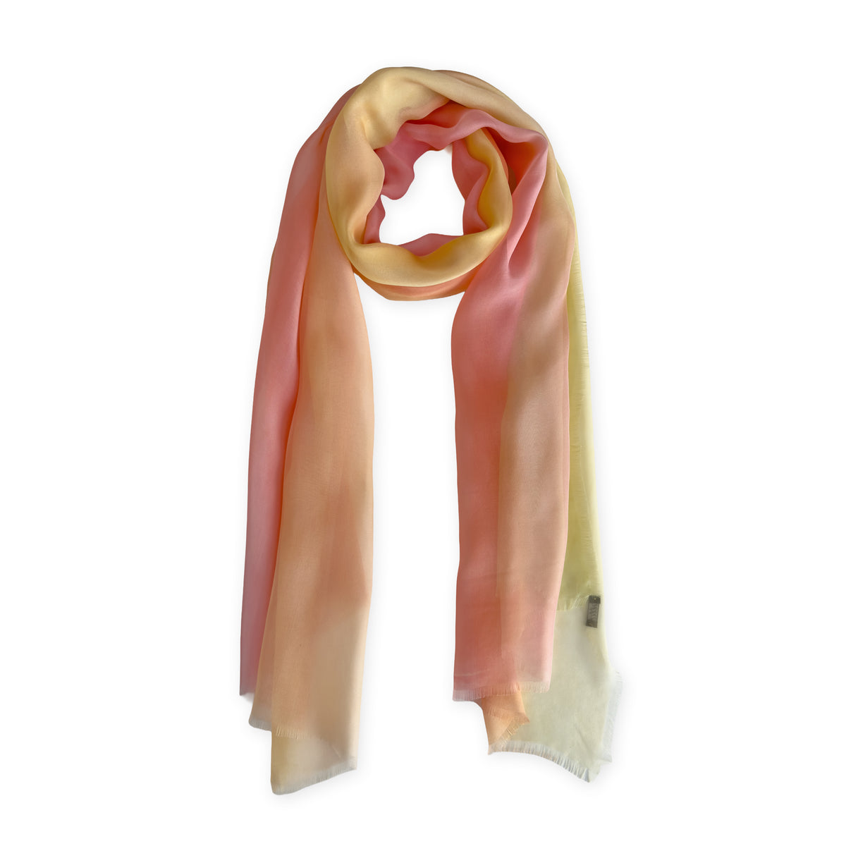 A hand-painted Otta pure silk scarf on a white background, in 
coral, peach, yellow and light green shades, loosely looped to showcase its full length and delicate texture. Lightweight artisan accessory with hand-fringed edges, measuring 65 x 175 cm.
