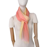 Mannequin wearing a hand-painted Otta pure silk scarf on a white background in 
coral, peach, yellow and light green tones. soft, fresh and lightweight, and elegant accessory measuring 65 x 175 cm. Unique artisan scarf with hand-fringed edges, perfect for women and men.
