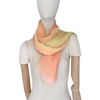 Mannequin wearing a hand-painted Otta pure silk scarf on a white background in 
coral, peach, yellow and light green tones. soft, fresh and lightweight, and elegant accessory measuring 65 x 175 cm. Unique artisan scarf with hand-fringed edges, perfect for women and men.
