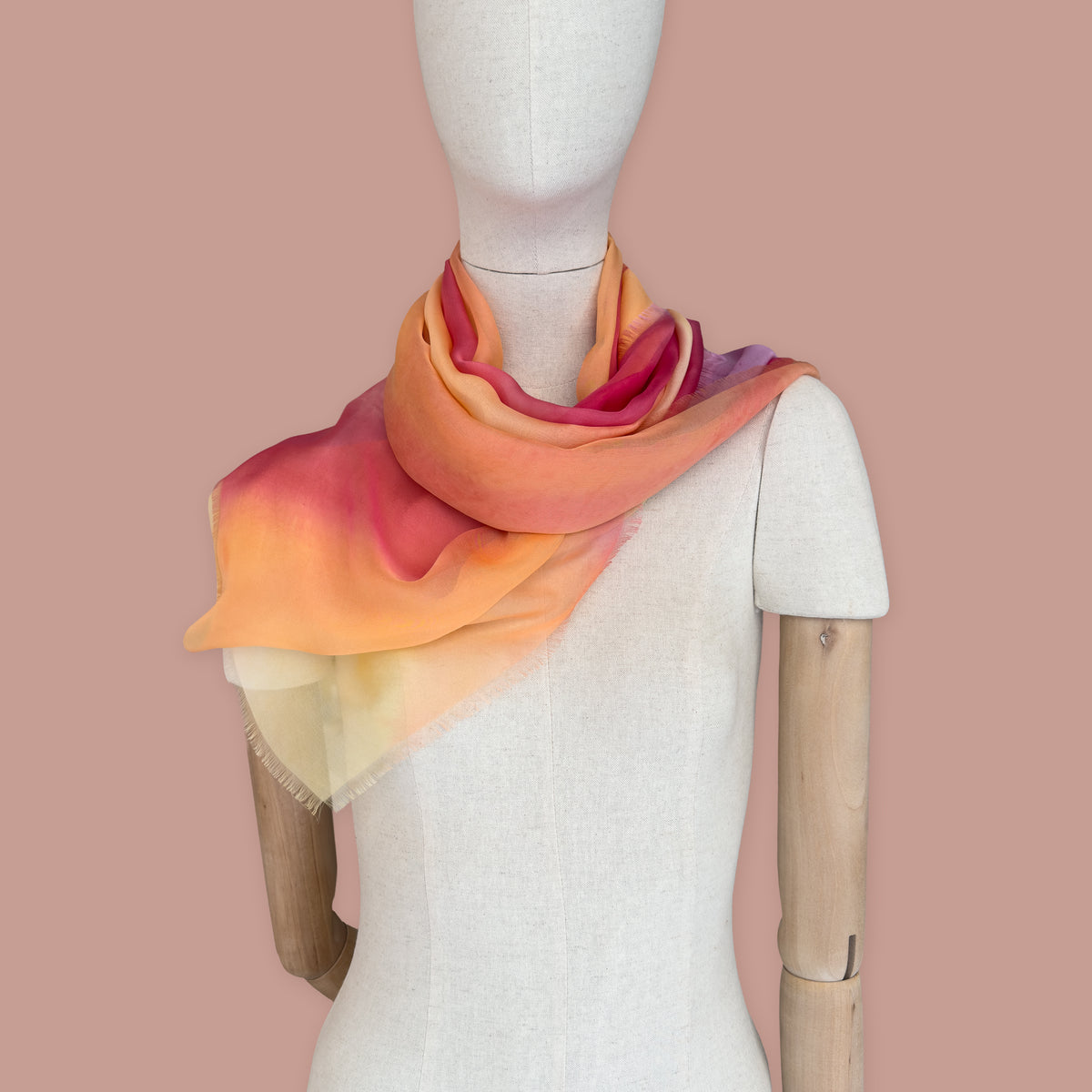 Mannequin wearing scarf on a peach color background. Hand-painted silk scarf by Otta-Italy, 65 x 175 cm, featuring 
red, orange, fuchsia and yellow. Luxury Italian pure silk accessory, soft, fresh and lightweight scarf for women and men.
