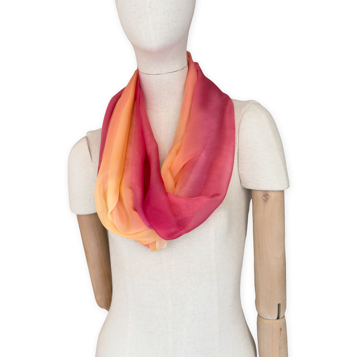 Mannequin wearing a hand-painted Otta pure silk scarf on a white background in 
red, orange, fuchsia and yellow tones. soft, fresh and lightweight, and elegant accessory measuring 65 x 175 cm. Unique artisan scarf with hand-fringed edges, perfect for women and men.

