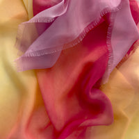 Close-up of a hand-painted Otta pure silk scarf draped softly, showcasing gentle shades of 
red, orange, fuchsia and yellow. Lightweight artisan accessory with delicate hand-fringed edges, measuring 65 x 175 cm.
