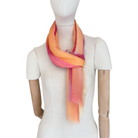 Mannequin wearing a hand-painted Otta pure silk scarf on a white background in 
red, orange, fuchsia and yellow tones. soft, fresh and lightweight, and elegant accessory measuring 65 x 175 cm. Unique artisan scarf with hand-fringed edges, perfect for women and men.

