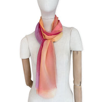Mannequin wearing a hand-painted Otta pure silk scarf on a white background in 
red, orange, fuchsia and yellow tones. soft, fresh and lightweight, and elegant accessory measuring 65 x 175 cm. Unique artisan scarf with hand-fringed edges, perfect for women and men.

