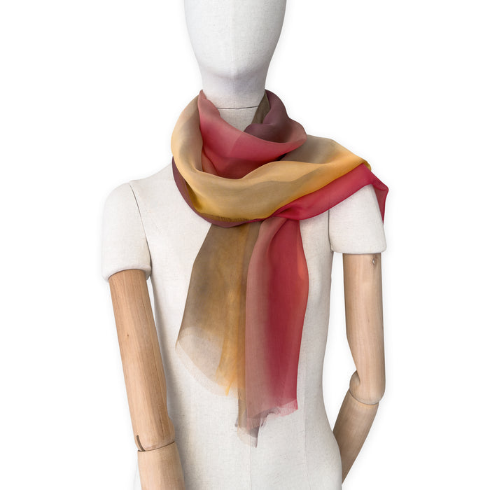 Mannequin wearing a colorful and lightweight silk scarf on a white background. Silk scarf is in shades of red, orange, yellow and brown colors. It is hand-painted scarf in measures 176 x 64 cm by otta-italy scarves brand.


