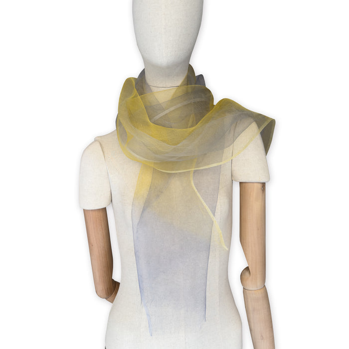 Mannequin wearing a colorful and lightweight silk scarf on a white background. Silk scarf is in shades of yellow and gray colors. It is hand-painted scarf in measures 50 x 194 cm by otta-italy scarves brand.

