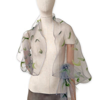 Mannequin wearing an elegant hand-painted Otta-Italy organic silk and wool felted scarf on a white background. Gray and green tones.
