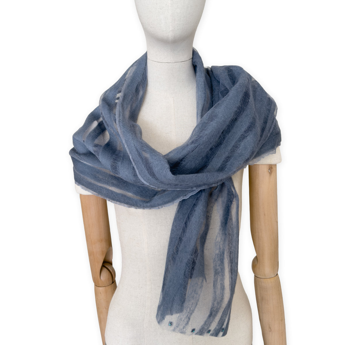 Mannequin wearing a hand-painted Otta pure silk with hand-needle felted wool scarf on a white background in 
gray tones. soft, fresh and lightweight, and elegant accessory measuring 40 x 176 cm. Unique artisan scarf with hand-fringed edges, perfect for women and men.
