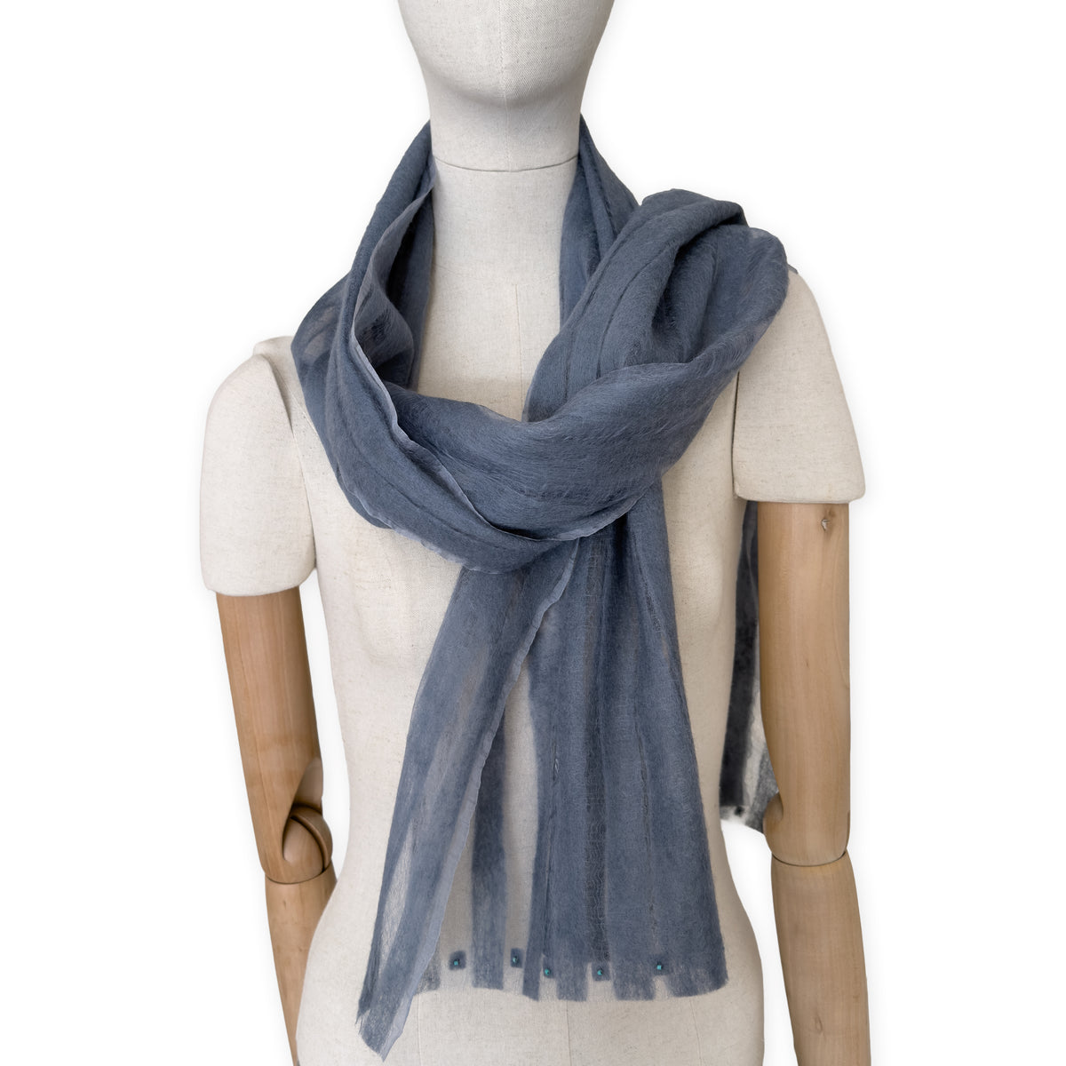 Mannequin wearing a hand-painted Otta pure silk with hand-needle felted wool scarf on a white background in 
gray tones. soft, fresh and lightweight, and elegant accessory measuring 40 x 176 cm. Unique artisan scarf with hand-fringed edges, perfect for women and men.
