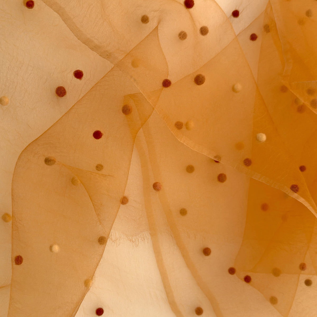 Close-up of a hand-painted Otta pure silk scarf draped softly with hand-needle felted wool showcasing gentle shades of 
orange, peach, beige and brown. Lightweight artisan accessory with delicate hand-fringed edges, measuring 183 x 44 cm.
