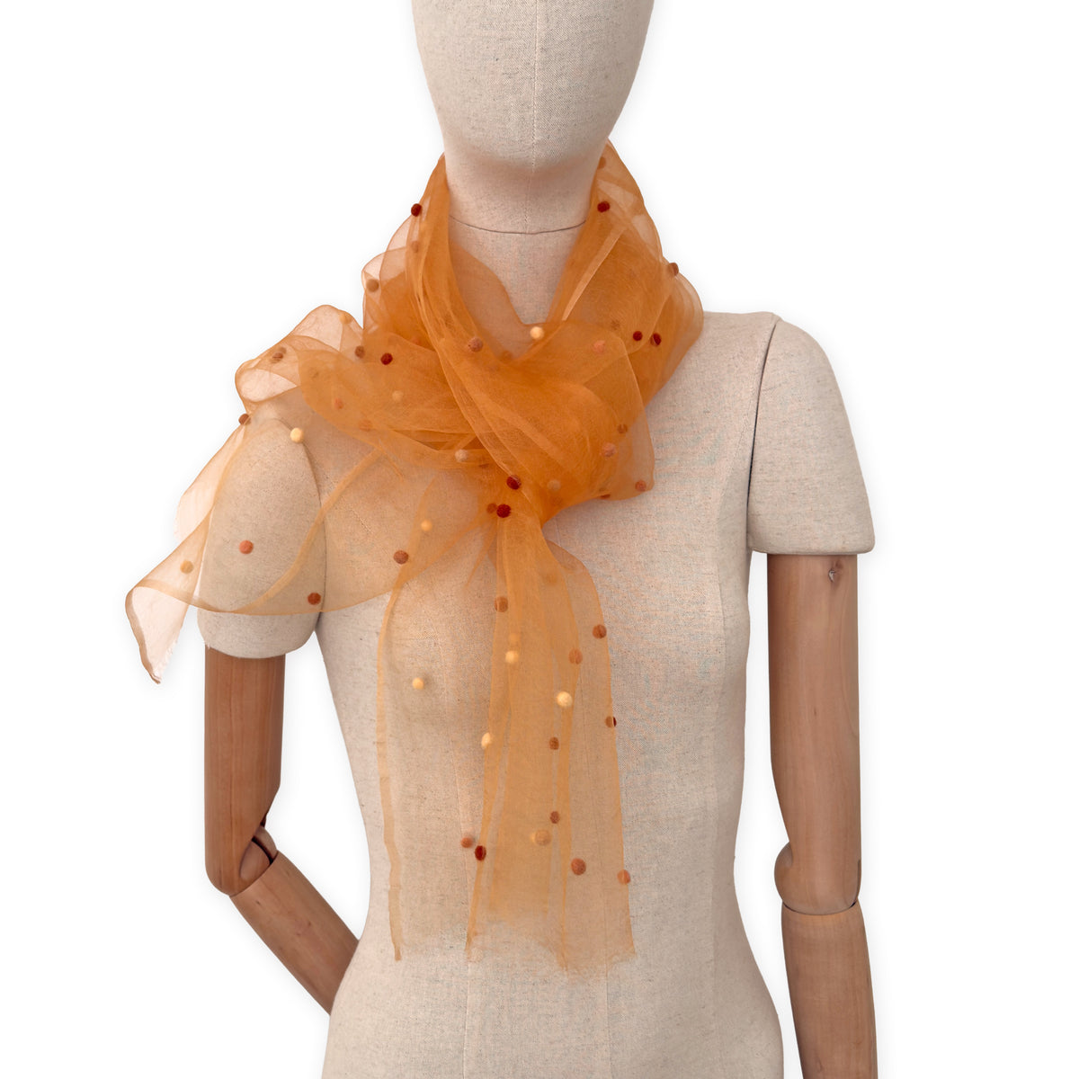 Mannequin wearing a hand-painted Otta pure silk with hand-needle felted wool scarf on a white background in 
orange, peach, beige and brown tones. soft, fresh and lightweight, and elegant accessory measuring 183 x 44 cm. Unique artisan scarf with hand-fringed edges, perfect for women and men.
