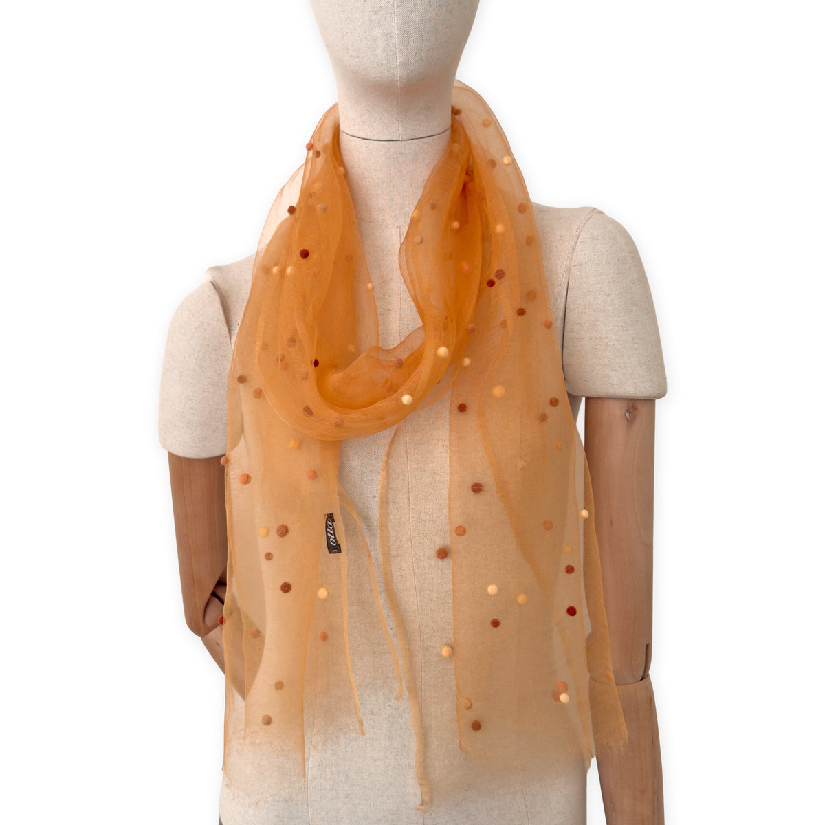 Mannequin wearing a hand-painted Otta pure silk with hand-needle felted wool scarf on a white background in 
orange, peach, beige and brown tones. soft, fresh and lightweight, and elegant accessory measuring 183 x 44 cm. Unique artisan scarf with hand-fringed edges, perfect for women and men.
