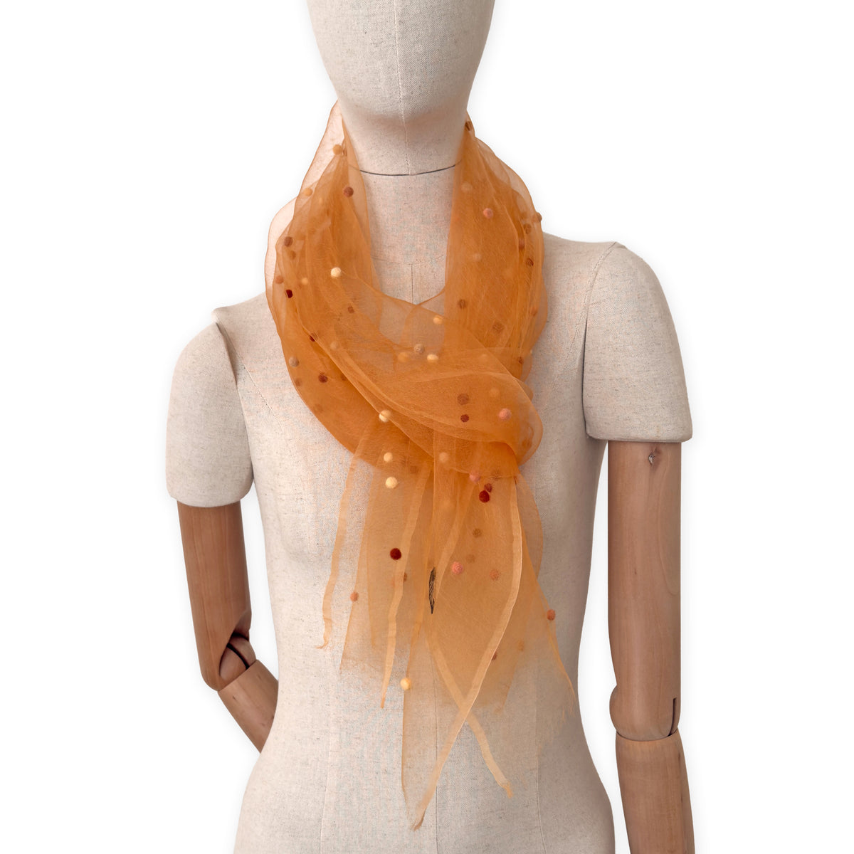 Mannequin wearing a hand-painted Otta pure silk with hand-needle felted wool scarf on a white background in 
orange, peach, beige and brown tones. soft, fresh and lightweight, and elegant accessory measuring 183 x 44 cm. Unique artisan scarf with hand-fringed edges, perfect for women and men.

