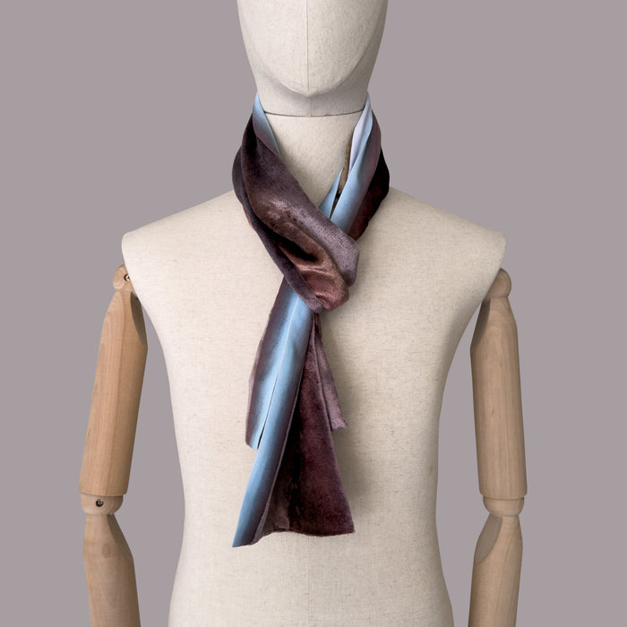 Mannequin wearing a colorful velvet scarf on a gray background. Velvet scarf is in shades of brown and blue colors. It is hand-painted scarf in measures 180 x 18 cm by otta-italy scarves brand.