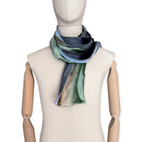 Mannequin wearing a colorful velvet scarf on a white background. Velvet scarf is in shades of green, beige and blue navy colors. It is hand-painted scarf in measures 182 x 18 cm by otta-italy scarves brand.

