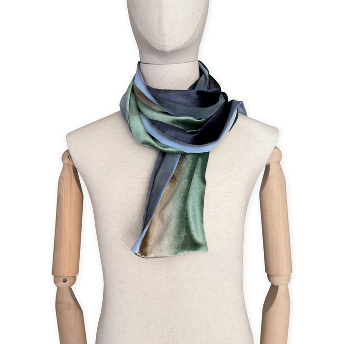 Mannequin wearing a colorful velvet scarf on a white background. Velvet scarf is in shades of green, beige and blue navy colors. It is hand-painted scarf in measures 182 x 18 cm by otta-italy scarves brand.
